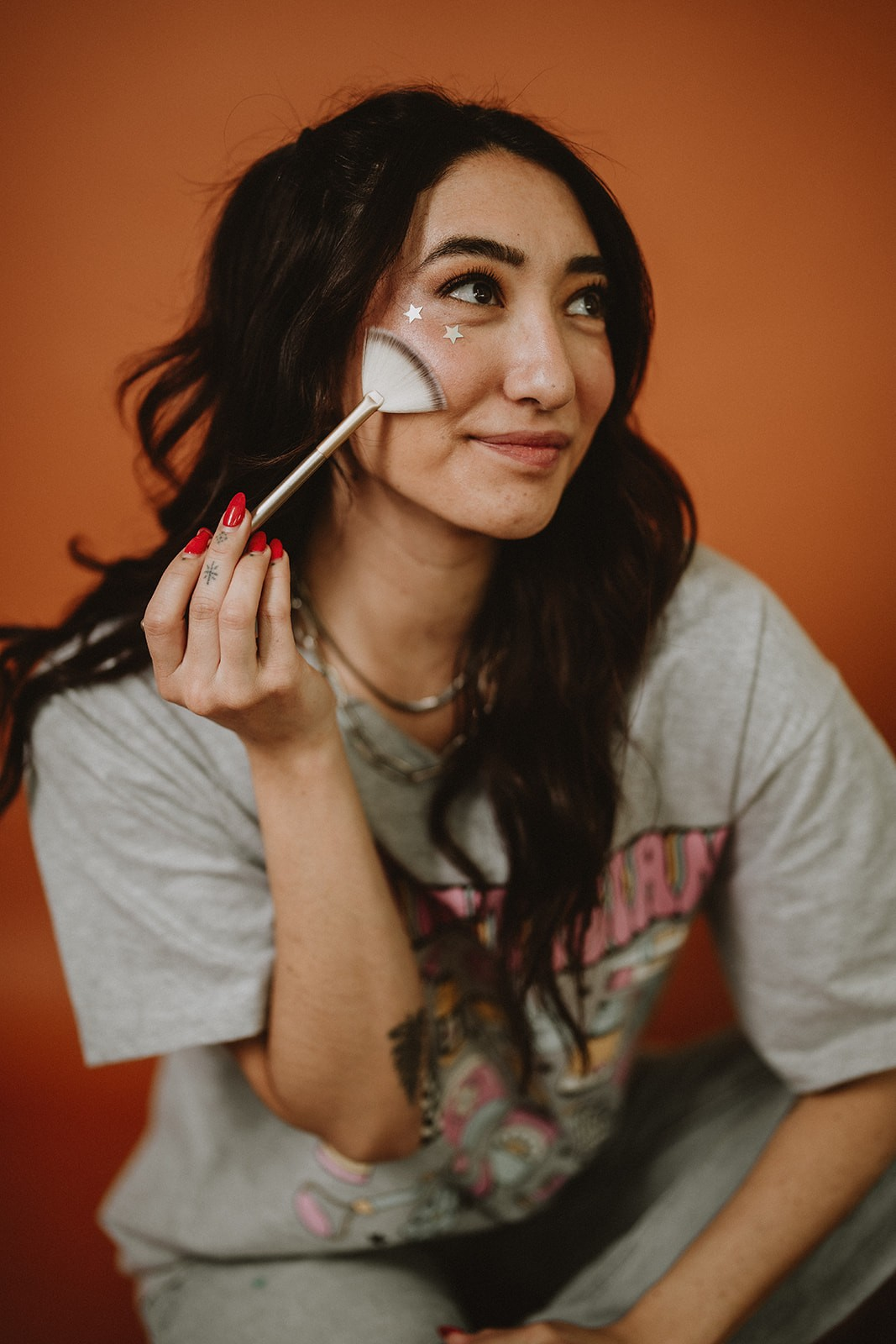 Tommi applying highlighter with a fan brush against a warm terracotta backdrop